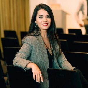 A person seated in an auditorium setting smiles toward the viewer