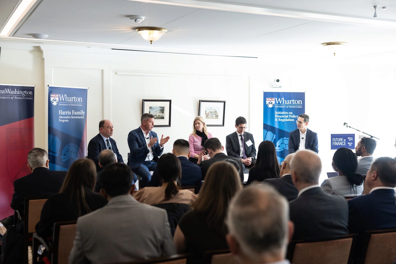 Five panelists seated before an audience at a conference