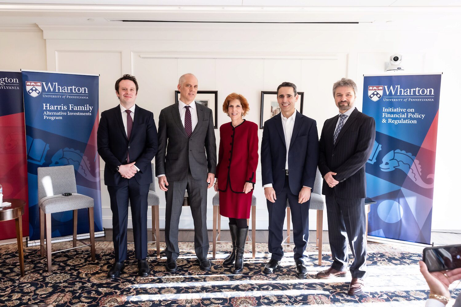 A group photo of five people posing in a sunlit room in between two blue pop-up banners.