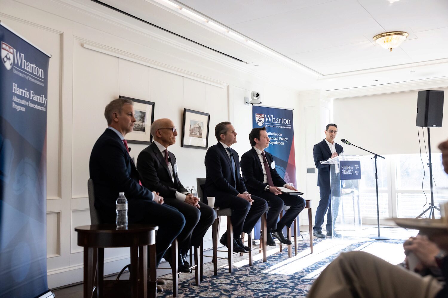 A speaker at a podium introduces a panel at a conference