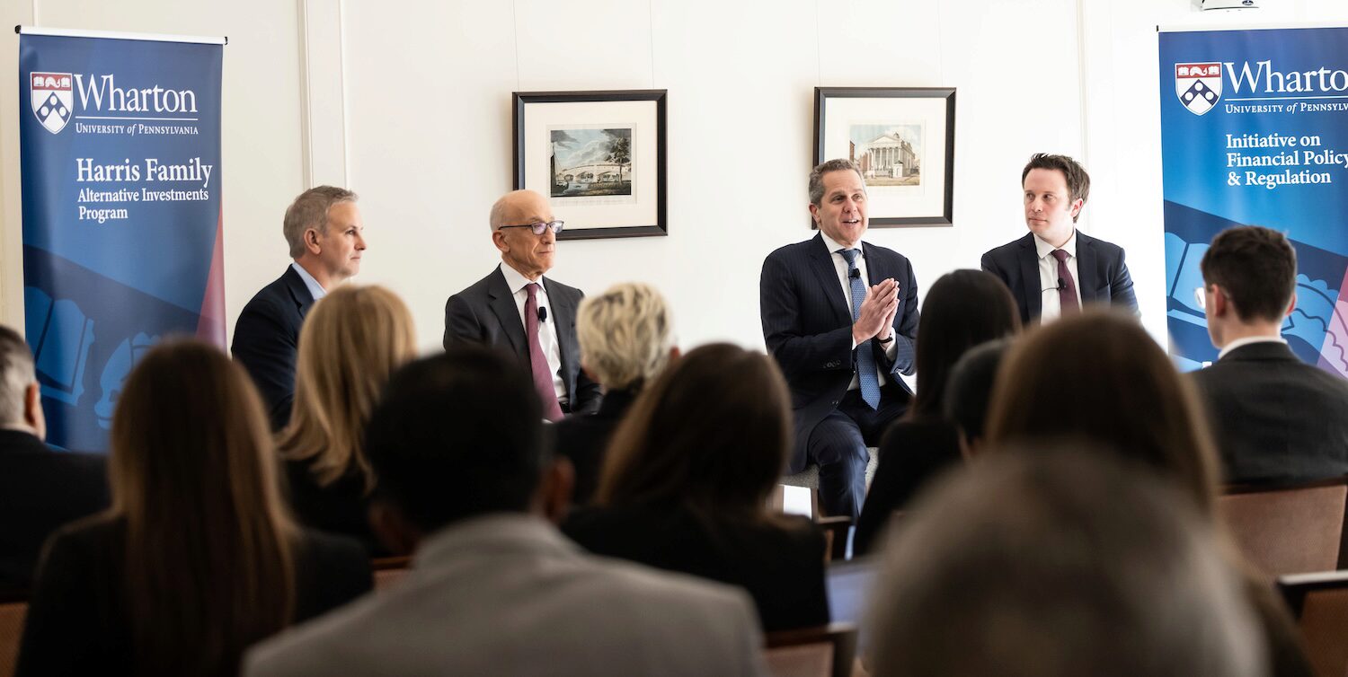 A panel at the Wharton Future of Finance Forum addresses the audience between two blue Wharton pop up banners