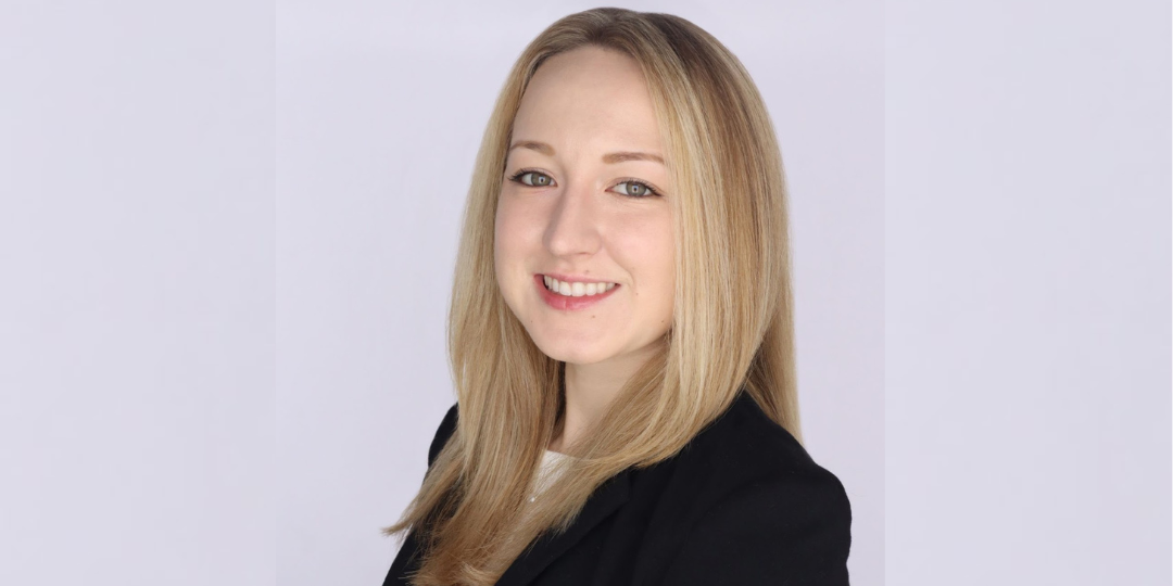 A person smiles toward the viewer in a professional headshot, before a light purple background