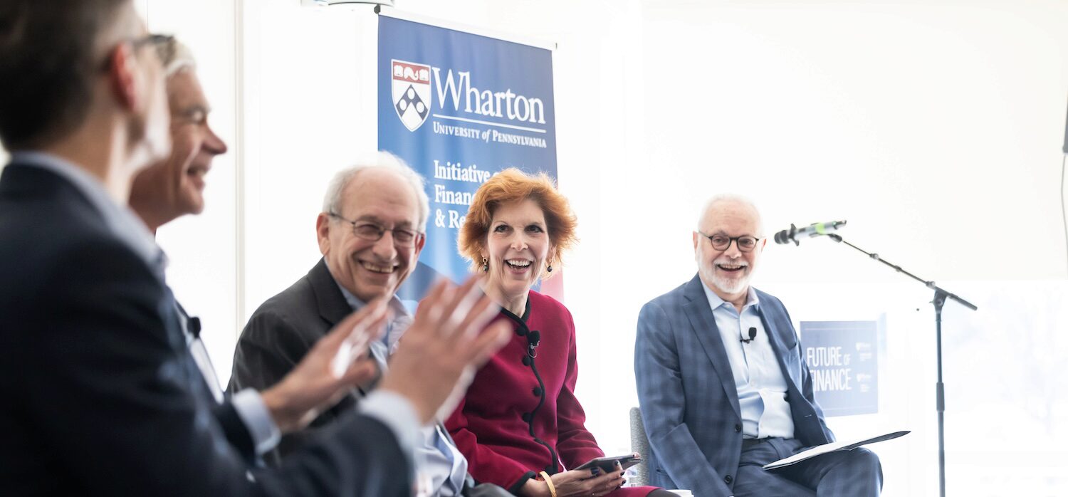A panel of speakers smiles while in conversation in a sunlit room