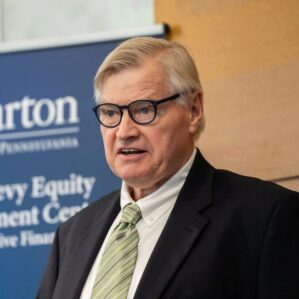 A person in a suit speaks before a blue banner